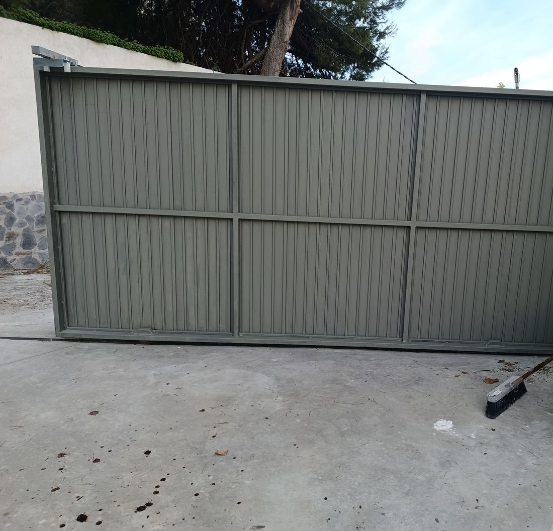 Cancela corredera de hierro con panel ciego, acabada en gris verdoso